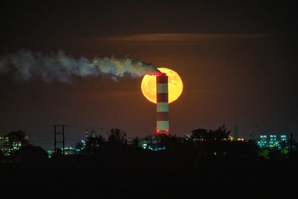 Wschodzący Księżyc za kominem Orlenu widzianym z Sikorza, z dymem płynącym w poprzek tarczy, 2 maja 2026.